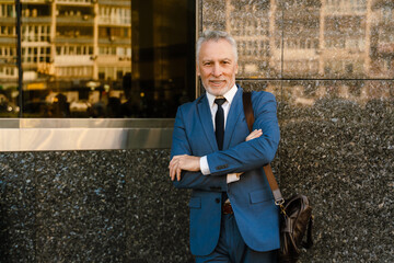 Senior man dressed in suit smiling while standing by building