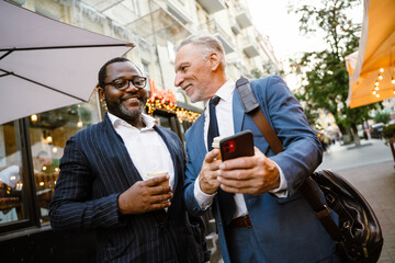 Multiracial two men using cellphone and talking while drinking coffee