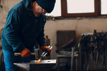 Blacksmith forges and makes metal detail with hammer and anvil at forge. Sparks and motion blur