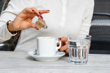 A woman adds cinnamon powder to her coffee on the table with a glass of pure water