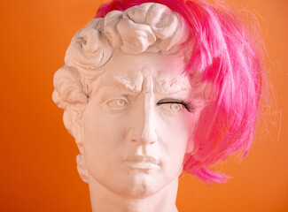 Plaster head of statue with pink wig and eyelashes. Man and  woman in half. Concept of gender identity.