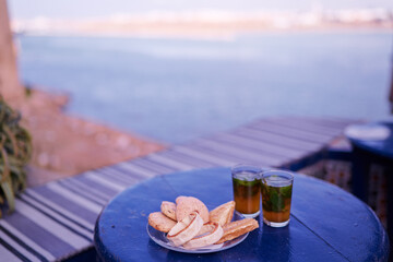 Moroccan mint tea and cookies on blue table with sea view.