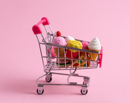 Shopping trolley full of sweets and fast food on pink background.