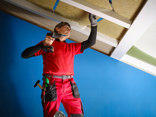 Rock wool applied to a wooden attic under renovation to save energy. Craftsman with work tools,...
