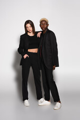 young brunette woman leaning on shoulder of blonde african american man on grey with shadow.