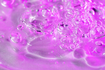 Facial serum drop with bubbles in bright pink neon light macro. Liquid bubbly anti aging gel...