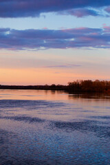 Sunset on Dnieper river. Beautiful dramatic cloudy sky and tree silhouettes reflecting in the water.