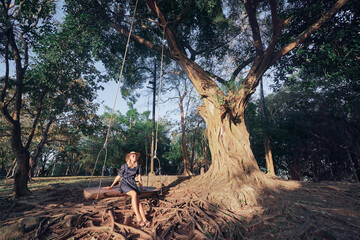 Vacation concept. Happy young woman in hat sitting in swing.