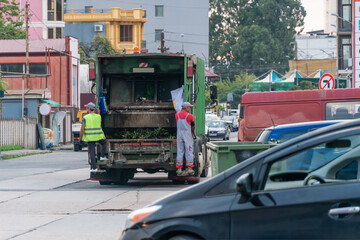 Two garbage men drive a garbage truck and collect garbage from containers in the city