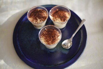 A shot of Tiramisu in small glass as a dessert on a blue plate with a spoon.