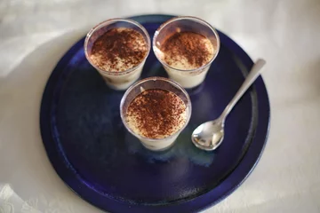 Fotobehang A shot of Tiramisu in small glass as a dessert on a blue plate with a spoon. © griangraf