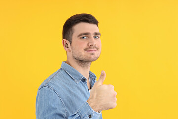 Young man with hearing aid on yellow background