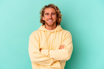 Young caucasian man isolated on blue background who feels confident, crossing arms with determination.