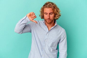 Young caucasian man isolated on blue background showing a dislike gesture, thumbs down....