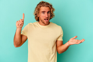 Young caucasian man isolated on blue background holding and showing a product on hand.