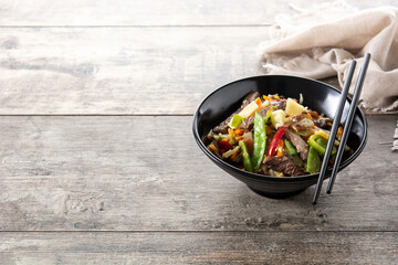 Beef, vegetables and sesame seeds in black bowl on wooden table. Copy space