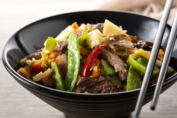Beef, vegetables and sesame seeds in black bowl on wooden table.