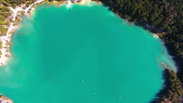 Former kaolin clay mine flooded by water. Few catamarans sailing around the surface. Green thick forests around. Top view.