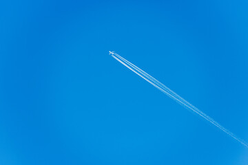A white Airliner with contrails flying in a clear blue sky, seen directly below, photography.