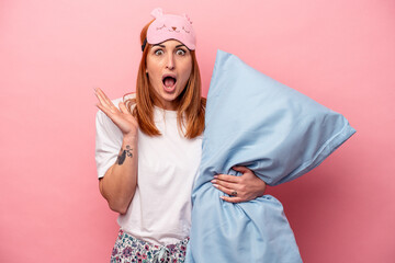 Young caucasian woman wearing a pajama holding pillow isolated on pink background surprised and shocked.