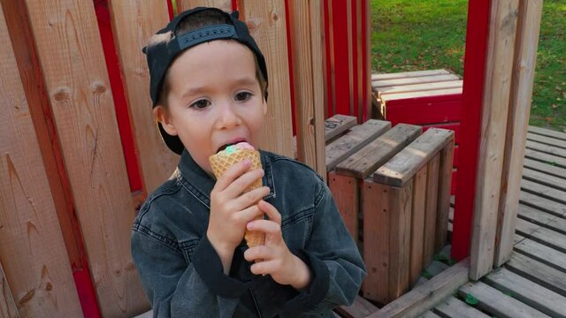 Beautiful boy caucasian preschool boy eating ice cream cone in Park .