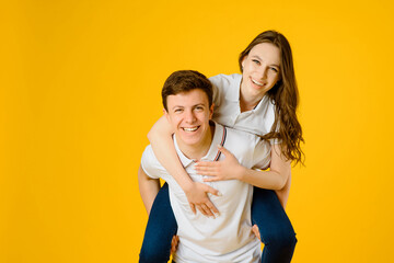 Fototapeta premium young happy couple man and woman in white t-shirts smiling and laughing on a yellow background..