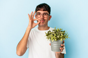 Young mixed race man holding a plant isolated on blue background with fingers on lips keeping a secret.