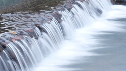 Long exposure on river flowing through rocks in forest, blurred motion.