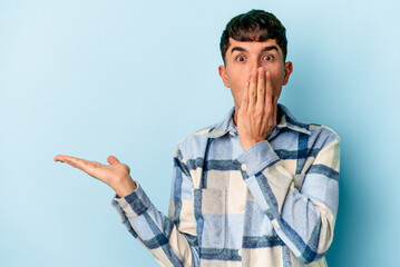 Young mixed race man isolated on blue background impressed holding copy space on palm.