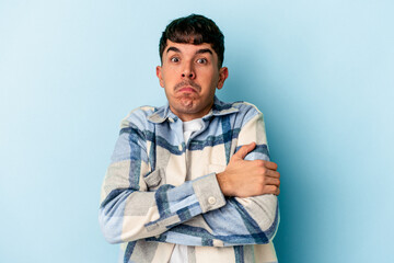 Young mixed race man isolated on blue background shrugs shoulders and open eyes confused.