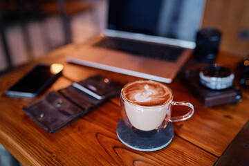 Traveler's breakfast. Cup of cappuccino on wooden table with laptop and photocamera.