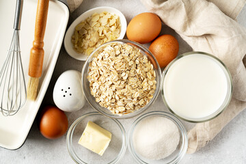 Ingredients for pudding or oatmeal pie on a light gray culinary background. Eggs, cereals, almonds, sugar, milk and butter on the kitchen table. Top view