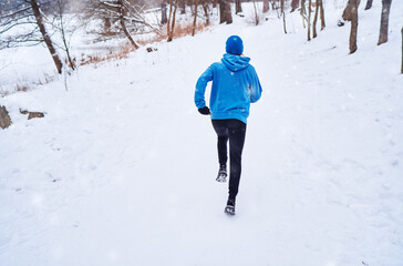 Healthy lifestyle. Jogging outdoors. Young strong man is running at snowy park.