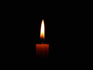 Candle flame on black background. Single lit candle with quite flame. Dramatic burning candle flame on a black background with copy space