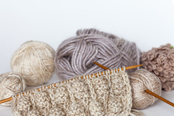 Close-up view of hand knitting on wooden needles and balls of woolen yarn on white background. Boucle, natural goat wool and wool/acrylic blend in beige and light tones. Knitting as hobby. DIY concept