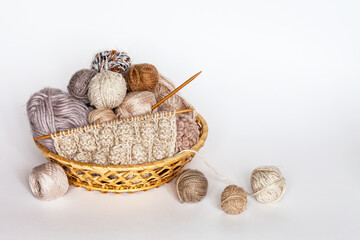 Wicker basket with different types of woolen yarn in pastel colors and knitted scarf on wooden...