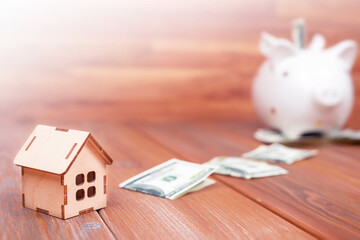 wooden house, dollars and a piggy bank on a wooden table