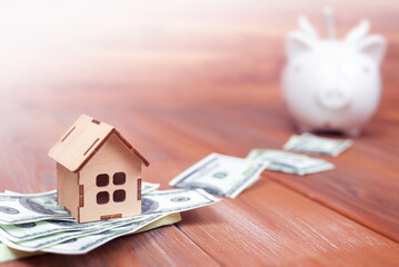 wooden house on a pack of dollars and a piggy bank on a wooden table