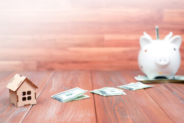 wooden house, dollars and a piggy bank on a wooden table