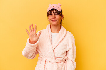 Young Argentinian woman wearing a pajama isolated on yellow background smiling cheerful showing number five with fingers.