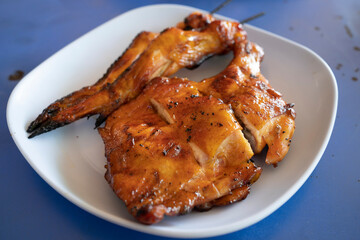 A large piece of grilled chicken is placed on a plate. in a local Thai restaurant