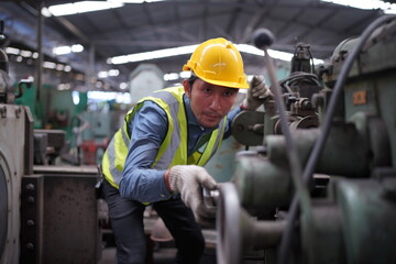 Male engineer metalworker industrial experienced operator technician worker in safety hard helmet working on lathe machine, professional man in industry technology manufacturing factory workshop