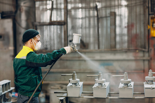 Powder primer coating of metal parts. Worker man in a protective suit sprays powder paint from gun on metal product construction at factory plant.
