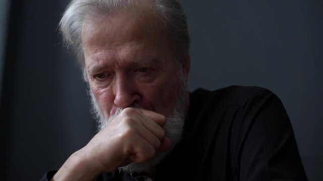 Close-up low-angle view of sad mature adult male remembering past life or youthfulness, widower mourns his wife feels miserable. Headshot of gray-haired aged man thinking of problem, sad memories.