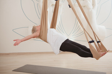 Happy healthy senior woman enjoying relaxing exercise on fly yoga hammock