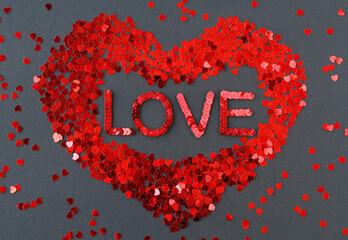 Inscription "Love" embroidered with red sequins inside a heart-shaped sequin heart on a black textured background