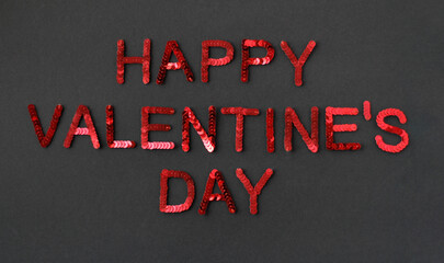 Inscription of "Happy Valentine's Day" embroidered with red sequins on black textured background as holiday decoration