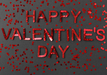 Inscription of "Happy Valentine's Day" embroidered with red sequins on black textured background with scattered random sequins in form of hearts