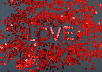 Inscription of "Love" embroidered with red sequins on black textured background with scattered random sequins in form of hearts
