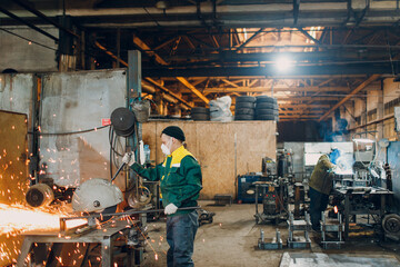 Workers working with metal construction on plant. Metal processing with big angle grinder disk saw and welder welding. Sparks in metalworking at factory.